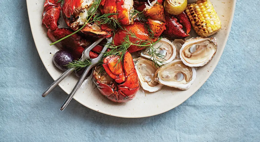 Coal-grilled lobsters served with charred corn, tomatillos, and blue potatoes on a rustic platter”